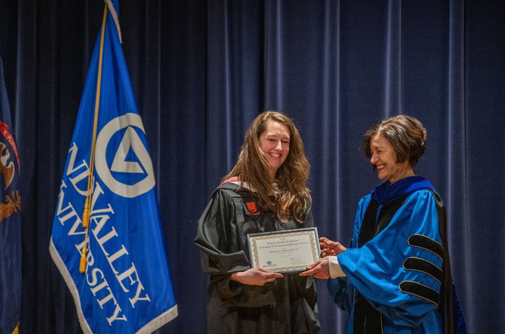 Provost Mili presents certificate to woman on stage